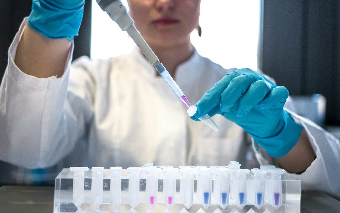 Scientist using a pipette over a rack of test tubes